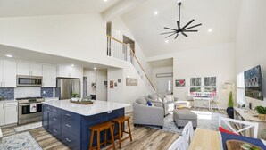 Una cocina amplia con una isla central, un comedor con una mesa de madera y una sala de estar con sofá y sillones.