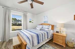 A bedroom with a bed, wooden nightstand, lamp, and a view of a field through a window.