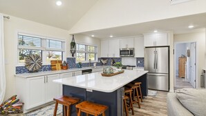 Una cocina amplia con una isla grande, armarios blancos y un refrigerador de acero inoxidable.