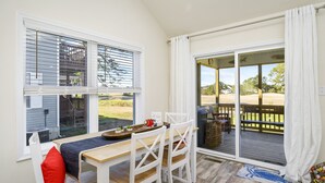Un comedor con una mesa y sillas, vistas al exterior a través de amplios ventanales y una terraza de madera.