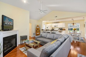 A living room with a gray sofa, a glass coffee table, a fireplace, and a kitchen in the background.