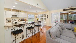 A spacious kitchen with white cabinets, a central island with bar stools, and a dining area with a view of the outdoors.