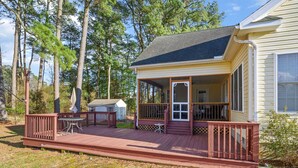 A wooden deck with a covered porch, a small shed, and a house with a large window.