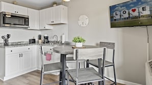 Cocina moderna con armarios blancos, microondas y comedor con mesa redonda y sillas de metal.