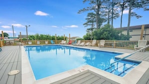 Una piscina rectangular con una terraza de madera, rodeada de sillas de descanso y una valla de madera.