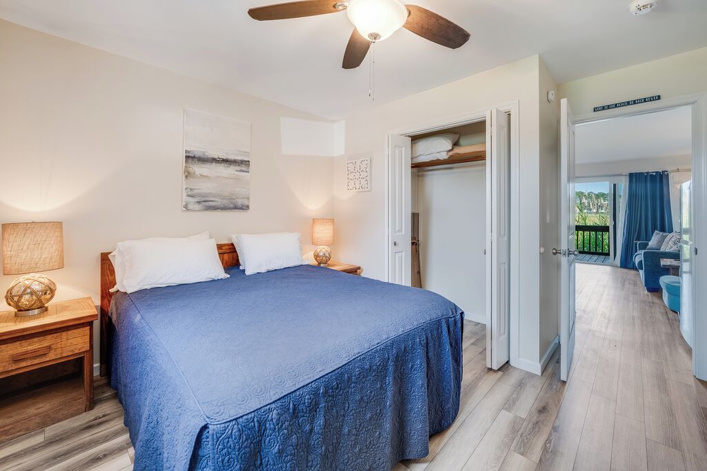 A bedroom with a bed, bedside lamps, a ceiling fan, and a view to a balcony.
