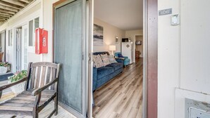 Une terrasse en bois avec une porte coulissante donnant sur une pièce où se trouvent un canapé bleu et une lampe.