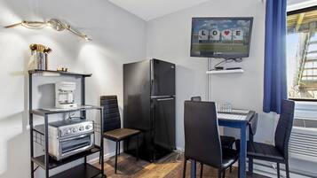 A compact kitchenette with a coffee maker, a refrigerator, and a TV mounted on the wall displaying "LOVE".