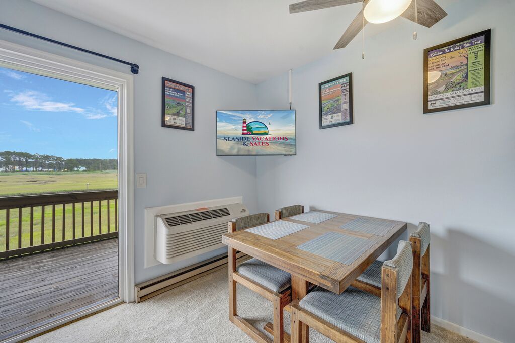 A room with a wooden table and chairs, a ceiling fan, and a large window overlooking a grassy area.