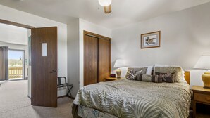 Ein Schlafzimmer mit einem Bett, zwei Nachttischen, einem Holzschrank, einer Tür zu einem Balkon und einem gerahmten Bild an der Wand.