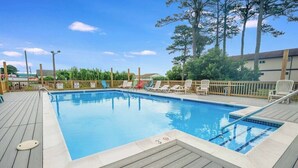 Une piscine rectangulaire dotée d’une terrasse en bois, entourée de chaises longues et d’une clôture en bois.