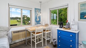 A compact kitchen with a dining area, large windows with views of greenery, a coffee maker, and a blue cabinet. - Assateague Inn 213 by Seaside Vacations & Sales (Chincoteague Island)
