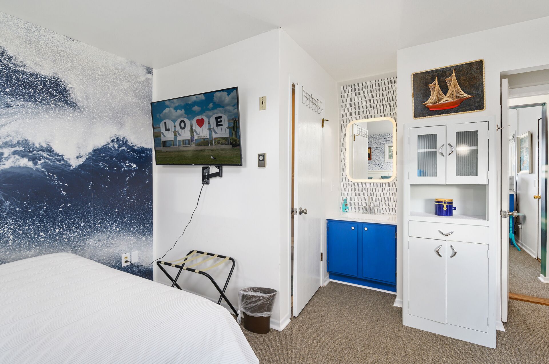 Une chambre à coucher avec un lit, un téléviseur fixé au mur, une armoire bleue et une porte dotée d’un miroir.