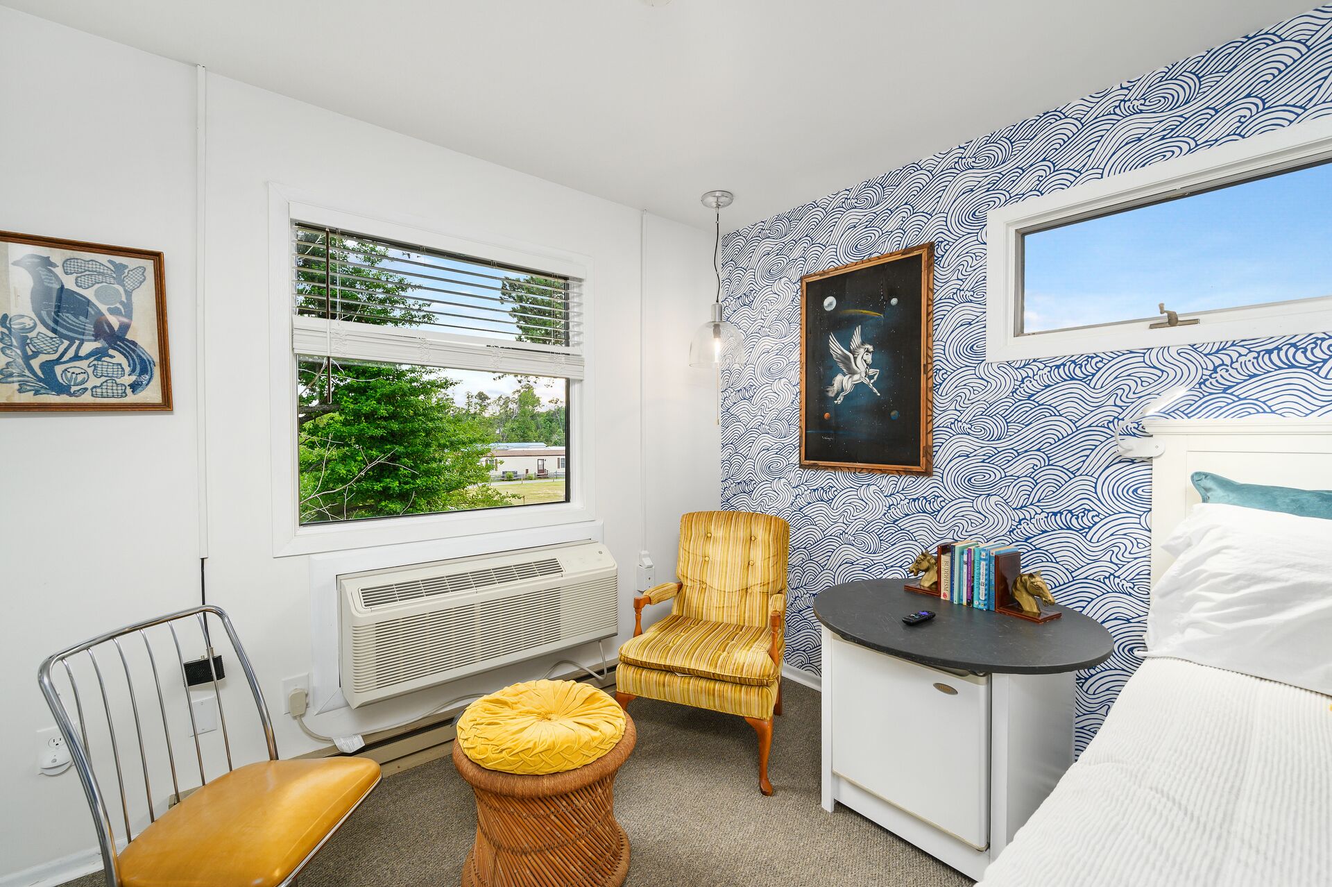 A room with a large window, a radiator, a chair, a small table, and a bed.
