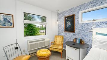 A room with a large window, a radiator, a chair, a small table, and a bed.