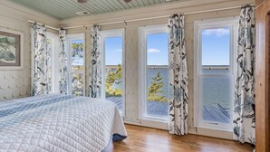 Un dormitorio con una cama grande, varias ventanas con cortinas, un ventilador de techo y vistas al exterior.