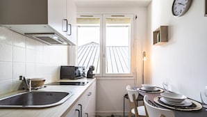 Een kleine keuken met witte kastjes, een ingebouwde magnetron, een spoelbak en een raam met uitzicht op een dak.