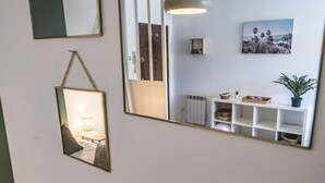 Een gang met een spiegel die een kamer weerspiegelt, een radiator, een plank met manden en een potplant.