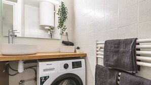 Een kleine badkamer met een wastafel, een wasmachine en een handdoekhouder.