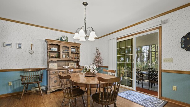 Un comedor con mesa y sillas de madera, una araña y vistas a un patio exterior a través de puertas de vidrio.