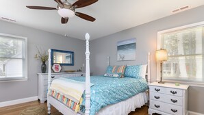 A bedroom with a four-poster bed, a nightstand with drawers, a lamp, and a window with blinds. - Teague Time by Seaside Vacations & Sales (Chincoteague)