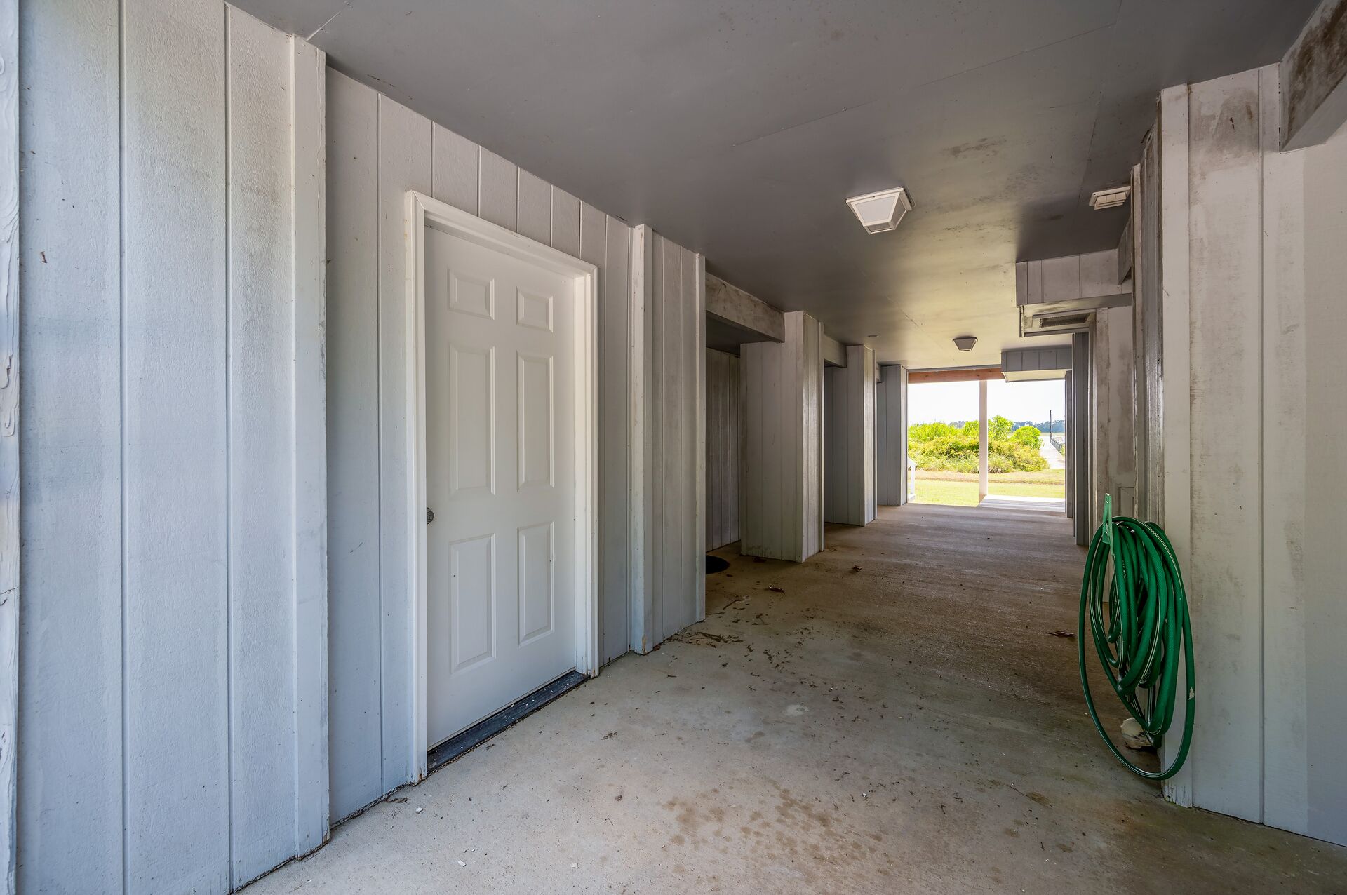 A hallway with white doors, a concrete floor, and a green garden hose.