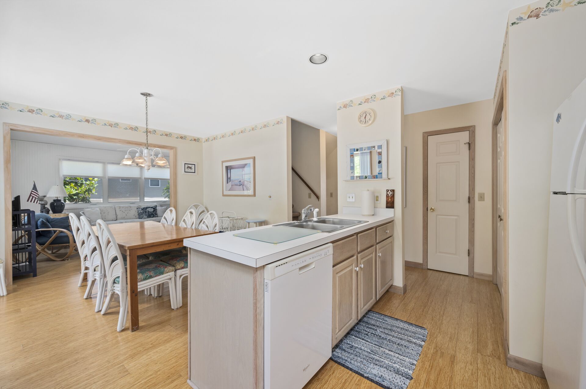 A compact kitchen with a central island, a dining area with white chairs, and a view of the outside through a window.