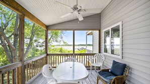 A covered porch with a table and chairs, a ceiling fan, and a view of a lake. - The Happy Crab by Seaside Vacations & Sales (Chincoteague Island)