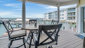 Um terraço coberto ao ar livre com mesa e cadeiras, com vista para uma marina com barcos e edifícios.