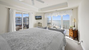 Een slaapkamer met een groot bed, een plafondventilator, een televisie en uitzicht op zee.