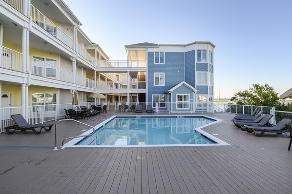 A pool area with lounge chairs and a pool, surrounded by multi-story buildings with balconies.