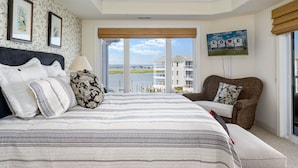 Ein Schlafzimmer mit einem großen Bett, Blick auf ein Gewässer und einem Balkon mit Blick auf Gebäude.