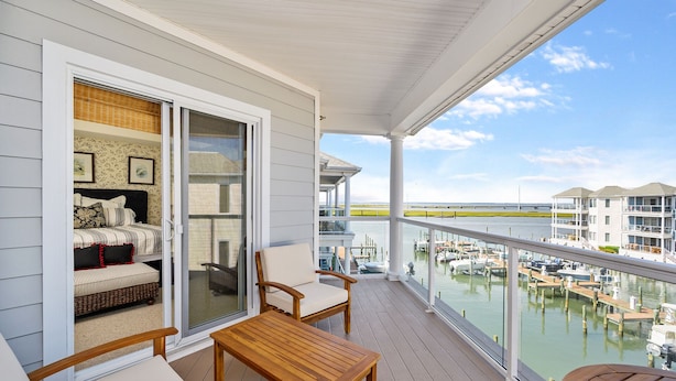 Ein Balkon mit Blick auf eine Marina, ein Bett mit gemusterten Betttextilien sowie ein Holztisch und Stühle.