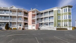 Un edificio residencial de varios pisos con balcones, estacionamiento y cielo despejado.
