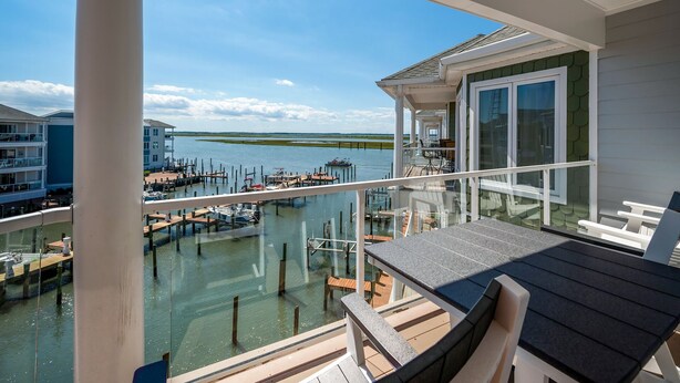 Un balcon donnant sur un port de plaisance, un espace repas avec des sièges en plein air et un bâtiment doté de grandes fenêtres.