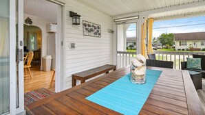 Eine überdachte Veranda mit Holztisch und -stühlen, einer Bank und Blick auf die Nachbarschaft.