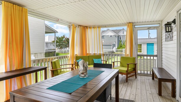 Eine überdachte Veranda mit einem Holztisch, grünen Stühlen und gelben Vorhängen.