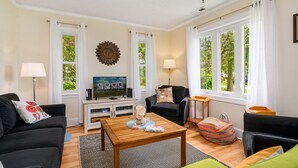 Ein Wohnzimmer mit Fernseher, Sofa, Couchtisch und Blick ins Grüne durch große Fenster.