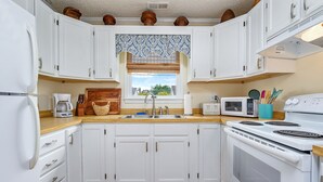 Eine Küche mit weißen Schränken, einer Holz Arbeitsplatte, einem Fenster mit gemustertem Vorhang und einer Mikrowelle, einem Toaster und einem Herd.