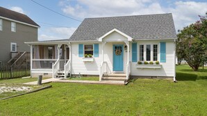 Ein eingeschossiges Haus mit einer Veranda, einer blauen Tür und einem kleinen Garten.