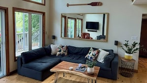 A spacious living room with a dark-colored sectional sofa, a wooden coffee table, and large windows with wooden frames. - Enjoy Beautiful Sunrise & Sunset in Your Private Island Paradise (Duoro-Dummer)