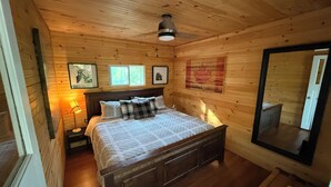 A wooden cabin bedroom with a bed, a nightstand, a lamp, and a large mirror. - Enjoy Beautiful Sunrise & Sunset in Your Private Island Paradise (Duoro-Dummer)