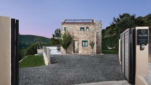 A stone building with a gravel driveway and a gate. - Villa Piedra (Platanias)