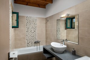 A modern bathroom with a freestanding bathtub, a large mirror, and a sink with a soap dispenser.