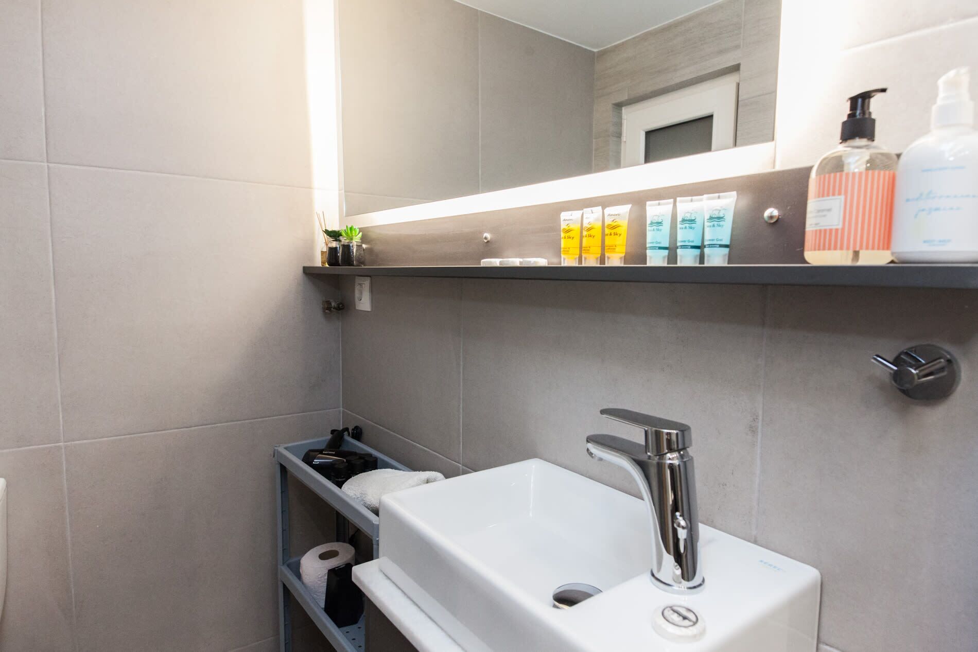 A modern bathroom with a white sink, a mirror, and a shelf with toiletries.