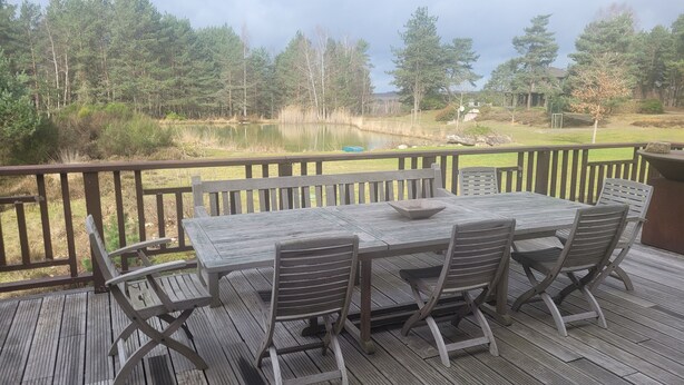 A wooden deck with a table and chairs, overlooking a pond and forested area. - Exceptional family lodge in the heart of nature, 60 kms from Paris. (LA BOISSIÈRE-ÉCOLE)