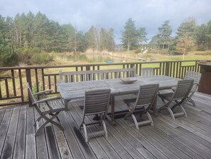 Um deck de madeira com mesa e cadeiras, com vista para um lago e área arborizada.