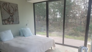 A bedroom with a large bed, a view of a forest through floor-to-ceiling windows, and a painting on the wall. - Exceptional family lodge in the heart of nature, 60 kms from Paris. (LA BOISSIÈRE-ÉCOLE)