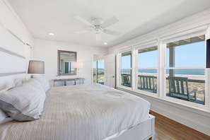 Une chambre à coucher avec un lit, un ventilateur de plafond, une table de chevet, une lampe, un miroir et une vue sur la plage.
