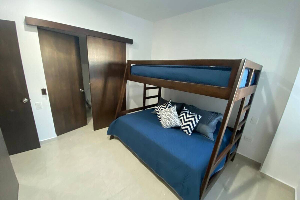 A bunk bed with a blue mattress and patterned pillows in a room with a tiled floor and wooden doors.